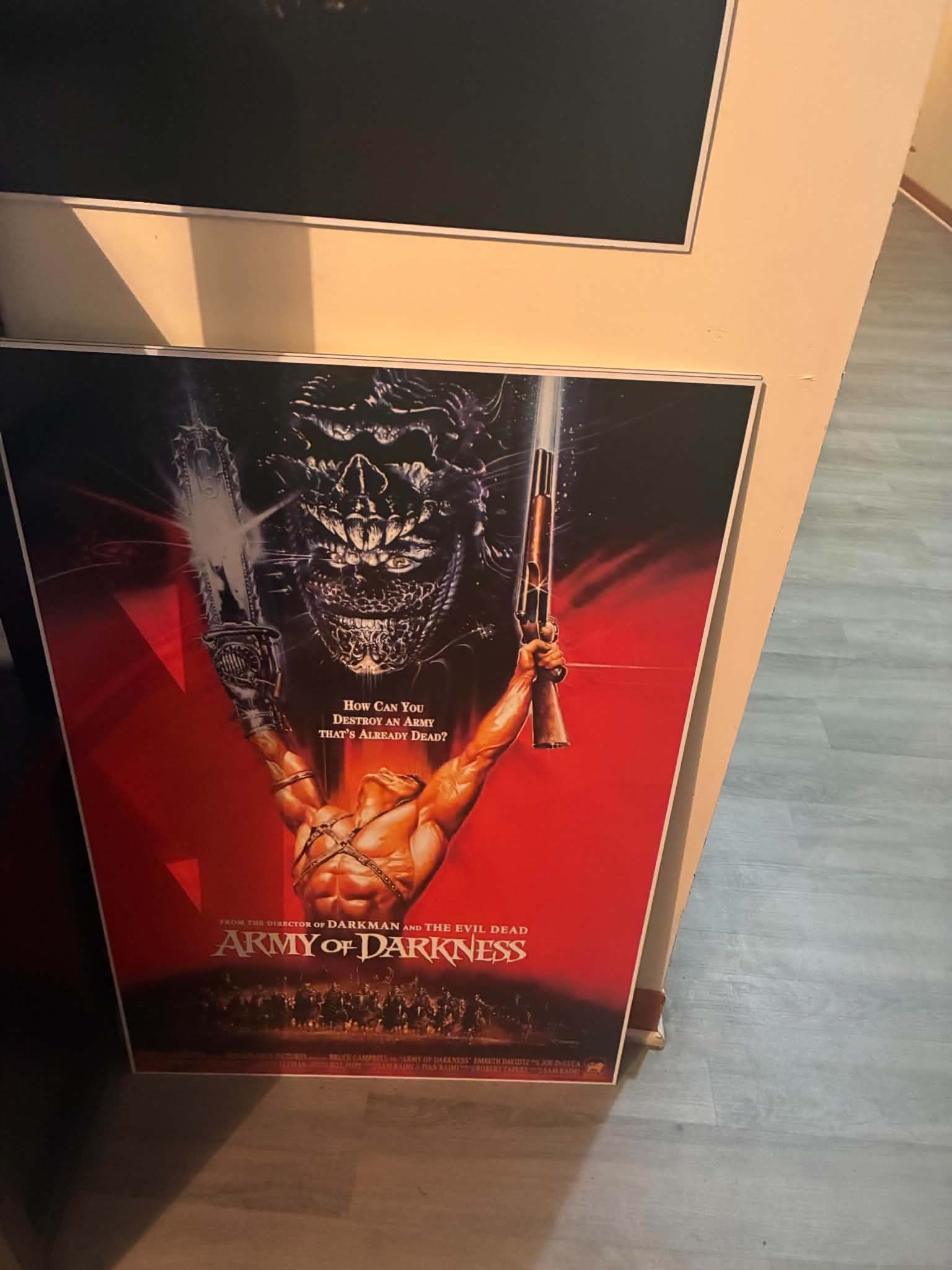 Photo of a red Army of Darkness print of Ash raising a chainsaw hand and a rifle before a giant demon face, tagline reads How can you destroy an army that's already dead?