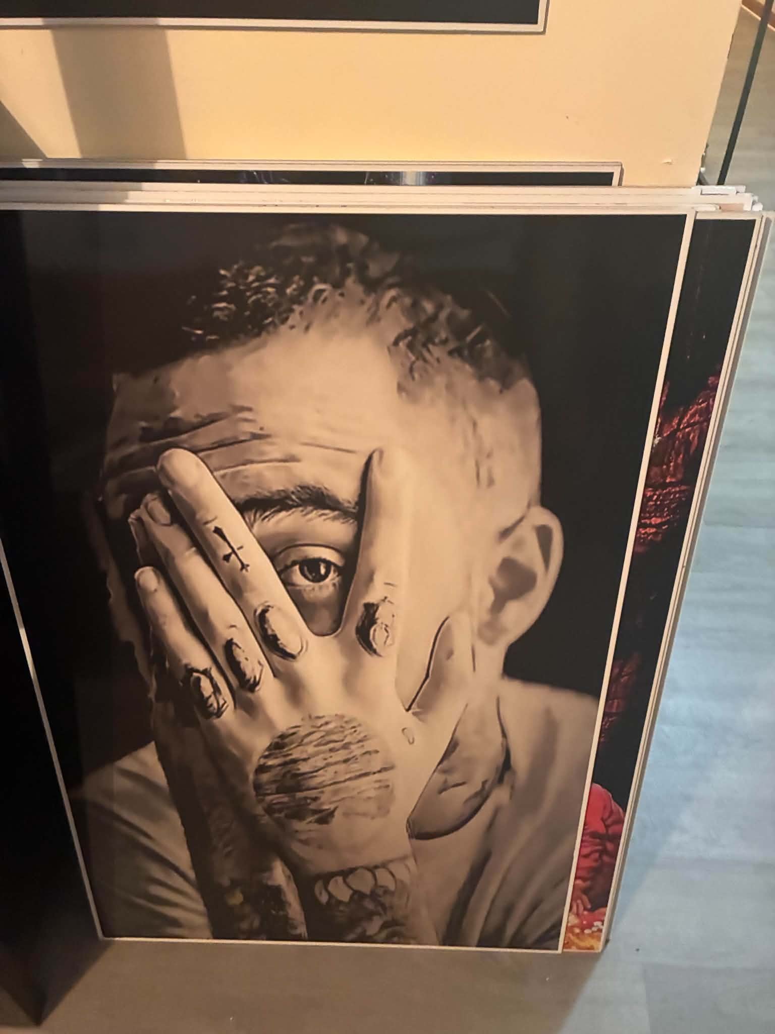Photo of a photorealistic black-and-white portrait print of a tattooed man partially covering his face with one hand